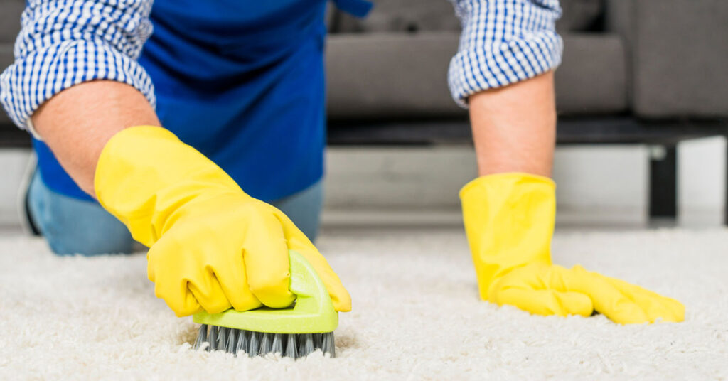 man wearing yellow gloves is cleaning the carpet with a small brush