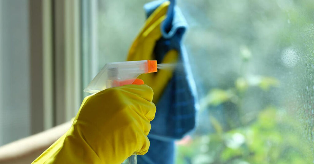 Cleaning a window with yellow gloves on while using a water spray