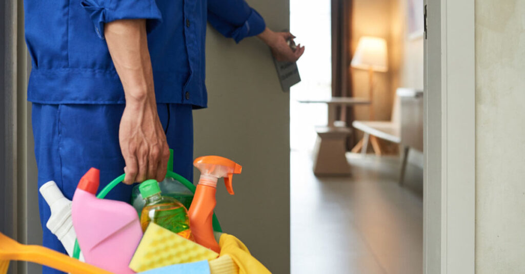 cleaner is opening the door while carrying a bucket of cleaning tools