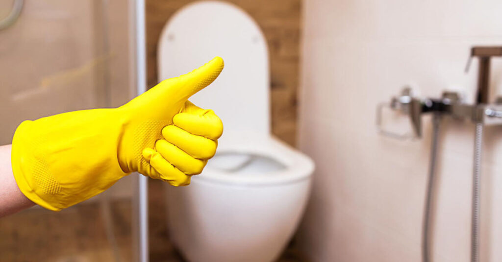 picture of a hand with a thumbs-up in a yellow glove against a bathroom background