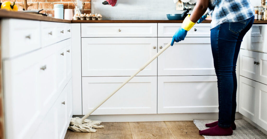 young woman with gloves on her hands, is sweeping the floor using a mop