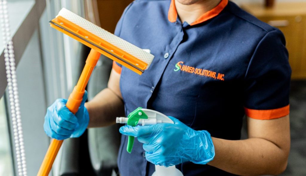 commercial cleaner holding cleaning materials, with window wiper and spray bottle in hand